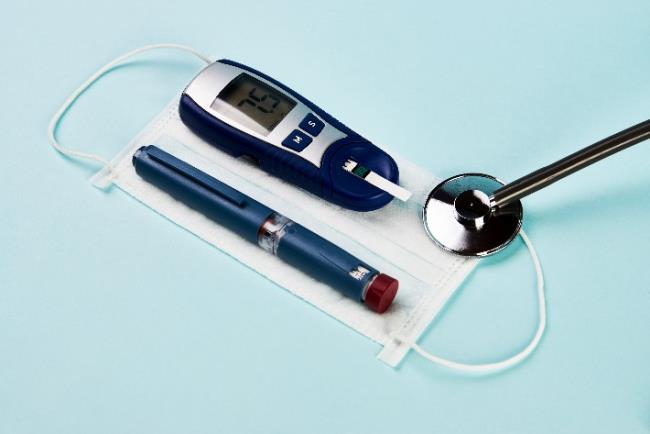 סוכרת בתקופת הקורונה: מזרק אינסולין ומד לניטור רמות סוכר בדם על גבי מסכה כירורגית